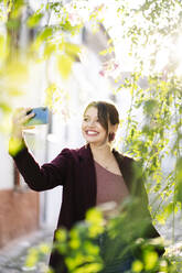 Lächelnde Frau macht ein Selfie in einer malerischen Gasse in der Stadt - DGOF00834