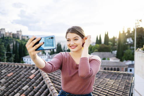 Porträt einer lächelnden Frau, die ein Selfie mit der Alhambra im Hintergrund macht, Granada, Spanien - DGOF00843