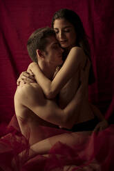 Intimate young couple hugging in front of ruby curtain - GMLF00022