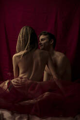 Intimate young couple hugging in front of ruby curtain - GMLF00030