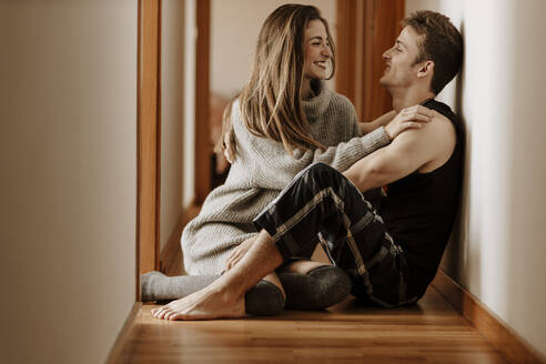 Happy young couple sitting on the floor at home - GMLF00059