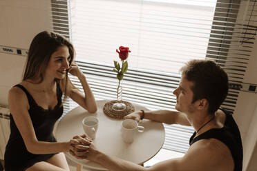 Romantisches junges Paar mit roter Rose am Küchentisch sitzend - GMLF00068