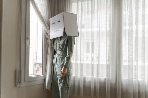 Woman wearing a cardbox on head with bored smiley looking out of the window stock photo