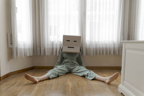 Woman wearing a cardbox on head with bored smiley sitting on the floor - AFVF06052