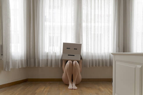 Woman wearing a cardbox on head with bored smiley and sitting on floor - AFVF06063