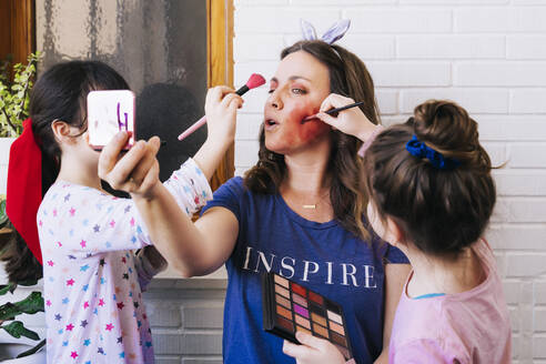 Töchter malen farbenfrohes Make-up auf das Gesicht der Mutter - ERRF03459