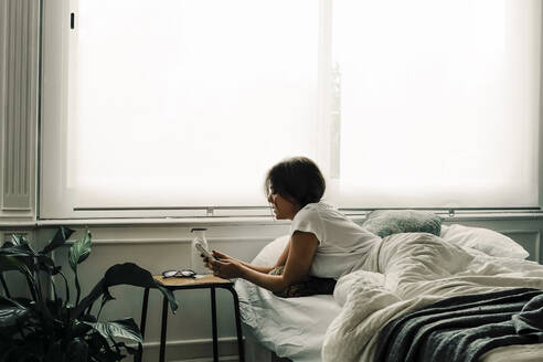Woman lying in bed in the morning checking cell phone - ERRF03467