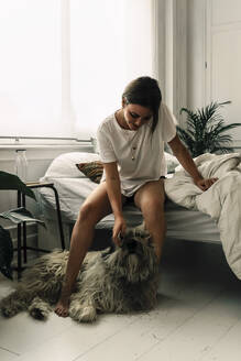 Mature woman standing up in the morning stroking her dog - ERRF03472