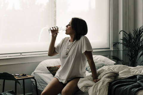 Mature woman sitting on bed in the morning drinking water stock photo