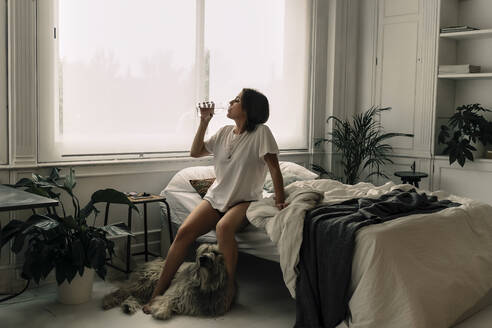 Mature woman sitting on bed in the morning drinking water - ERRF03474