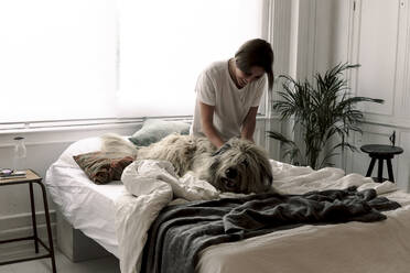 Happy mature woman cuddling her dog on bed - ERRF03476