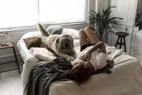 Mature woman lying on bed playing with her dog - ERRF03478