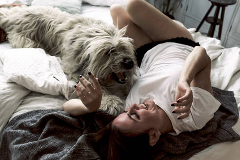 Mature woman lying on bed playing with her dog - ERRF03479