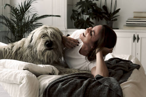 Laughing mature woman lying on bed having fun with her dog - ERRF03482