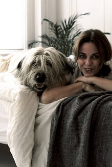 Porträt einer lächelnden reifen Frau auf dem Bett liegend mit ihrem Hund - ERRF03484