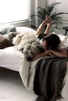 Reife Frau liegt auf dem Bett mit ihrem Hund und entspannt sich - ERRF03486