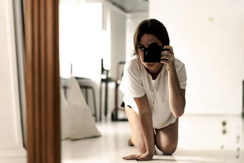 Mirror image of mature woman kneeling on floor taking photo with camera - ERRF03490