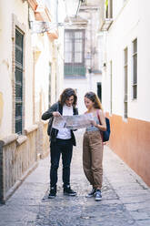 Paar in voller Länge beim Lesen einer Landkarte auf einer engen Straße in Santa Cruz, Sevilla, Spanien - DGOF00862