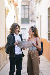 Glückliches junges Paar mit Landkarte in einer engen Straße in Santa Cruz, Sevilla, Spanien - DGOF00865