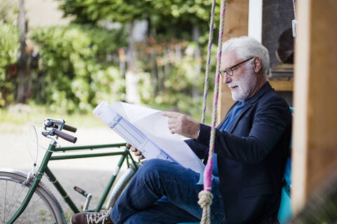 Älterer Mann sitzt im Freien und betrachtet einen Bauplan, lizenzfreies Stockfoto