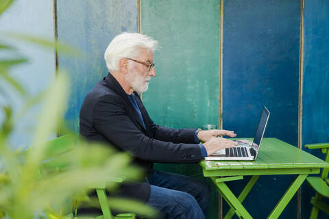 Senior man sitting at table outdoors using laptop stock photo