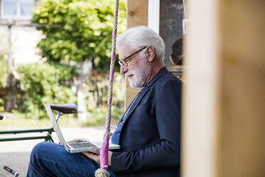 Älterer Mann sitzt im Freien und schaut auf einen Laptop - JOSEF00262