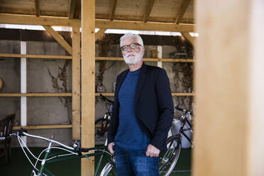 Portrait of senior man sitting with racing cycle standing in a shelter - JOSEF00266
