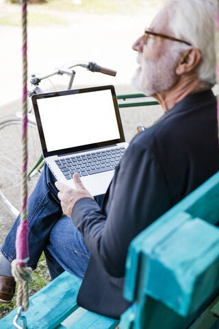 Senior man sitting outdoors using laptop stock photo