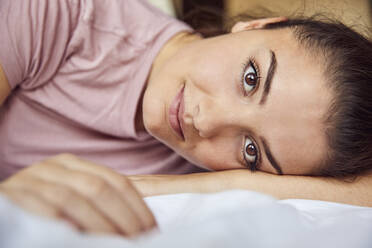 Porträt einer jungen Frau mit braunen Augen auf dem Bett liegend - JHAF00119
