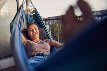 Portrait of happy young woman relaxing on hammock on balcony - JHAF00123