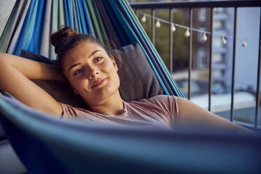 Portrait of smiling young woman relaxing on hammock on balcony - JHAF00125