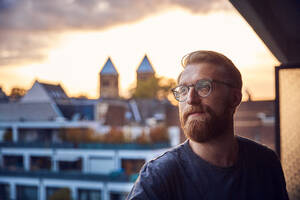 Porträt eines nachdenklichen Mannes auf einem Balkon mit Blick in die Ferne - JHAF00143