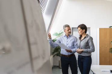 Businessman and businesswoman discussing paper in office - DIGF09675