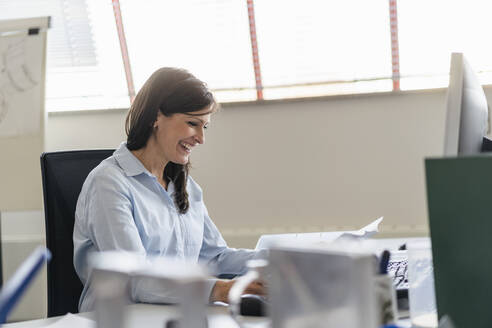 Glückliche Geschäftsfrau bei der Arbeit am Schreibtisch im Büro - DIGF09689