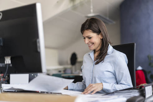 Lächelnde Geschäftsfrau bei der Arbeit am Schreibtisch im Büro - DIGF09690