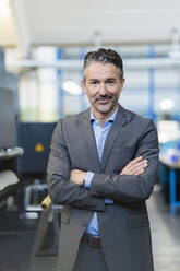 Portrait of successful businessman in shop floor of company, with arms crossed - DIGF09707