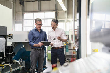 Geschäftsleute in einer Fabrik, die eine Besprechung haben und ein digitales Tablet benutzen - DIGF09760