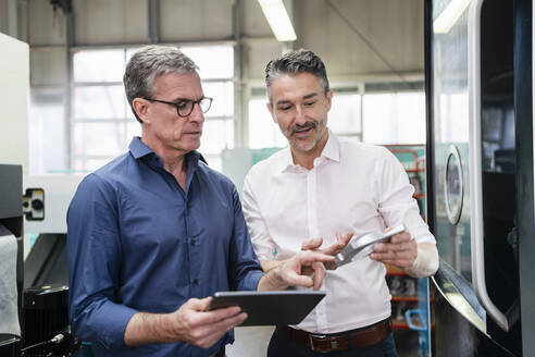 Geschäftsleute in einer Fabrik, die eine Besprechung haben und ein digitales Tablet benutzen - DIGF09765