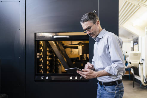 Älterer Mann bei der Arbeit in der Produktionshalle einer Fabrik, der ein digitales Tablet benutzt - DIGF09804