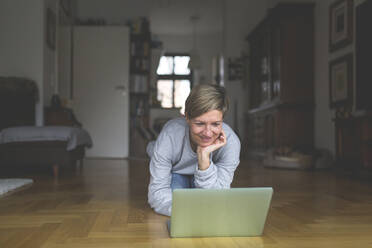 Mature woman working from home, using laptop, kneeling on floor - ASCF01238