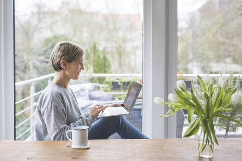 Reife Frau, die von zu Hause aus arbeitet, mit Laptop, auf einer Bank sitzend - ASCF01247