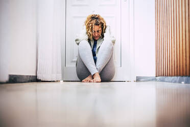 Verzweifelte Frau sitzt auf dem Boden im Korridor vor verschlossener Tür - SIPF02153