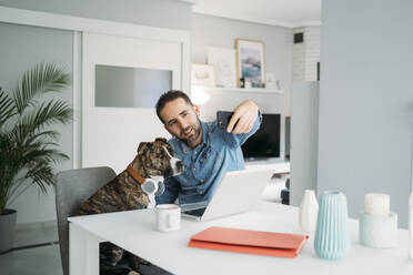 Ein mittelgroßer Mann macht ein Selfie mit seinem Hund, während er während der Coronavirus-Krise von zu Hause aus arbeitet, Almeria, Spanien, Europa - MPPF00852