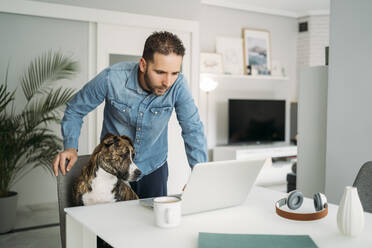 Man standing by dog while using laptop from home during coronavirus pandemic outbreak, Almeria, Spain, Europe - MPPF00854
