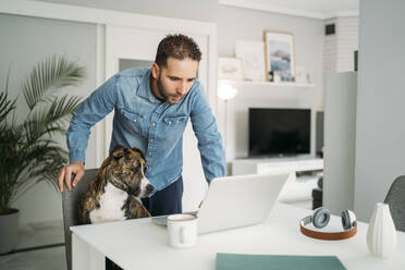 Mann steht neben seinem Hund und benutzt seinen Laptop während des Ausbruchs der Coronavirus-Pandemie, Almeria, Spanien, Europa - MPPF00854