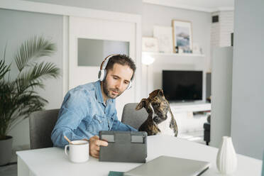 Mann zeigt seinem Hund ein digitales Tablet, während er während der Coronavirus-Quarantänezeit von zu Hause aus arbeitet, Almeria, Spanien, Europa - MPPF00859