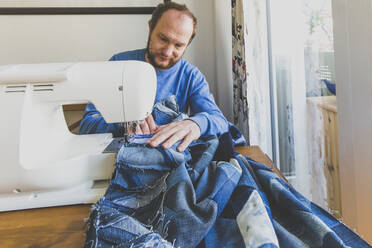 Mature man sewing denim quilt at home - IHF00336