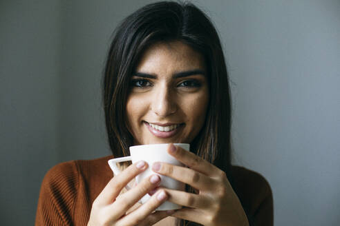 Portrait of smiling businesswoman enjoying coffee in break at office - ABZF03090