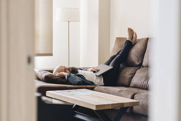 Man taking nap while lying with laptop on sofa at home - DGOF00894