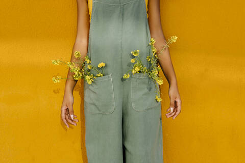 Midsection of woman wearing overalls with yellow flowers in pockets stock photo